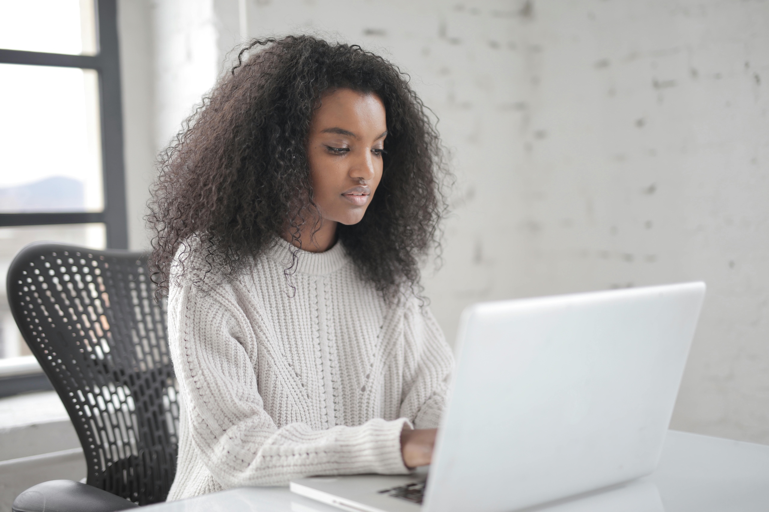A woman smiling while working on her laptop in a bright, modern office, symbolising calm and balanced productivity. Achieving a work life balance